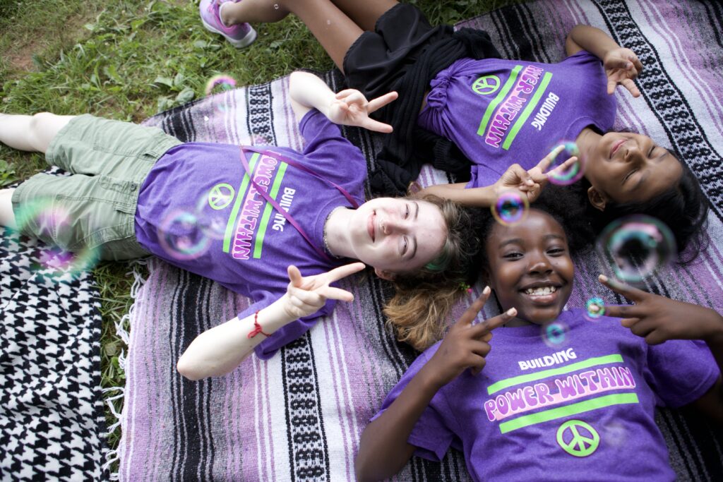 Campers in Camp PEACE shirts lying on a blanket and smiling up at the camera