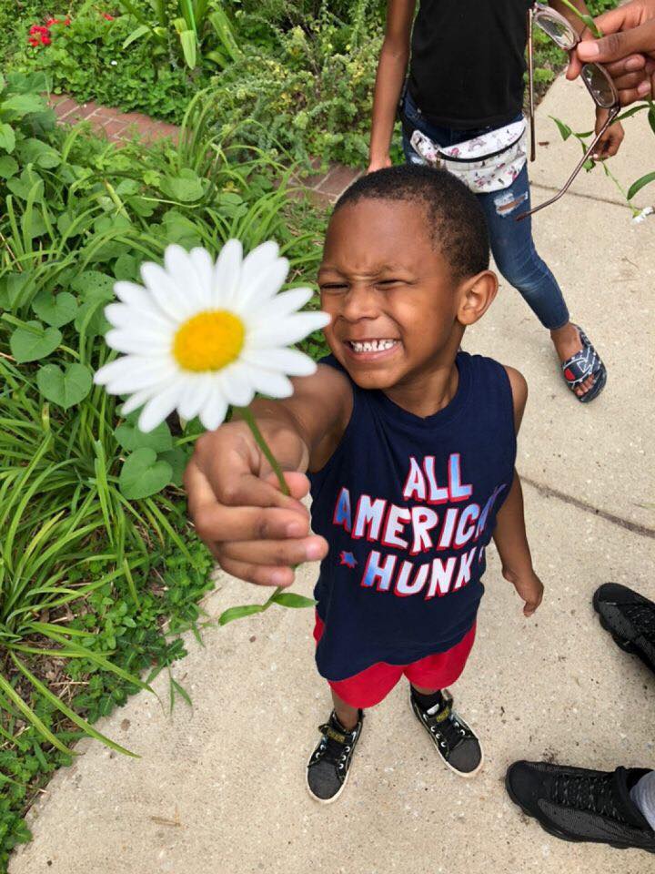 A smiling young camper holding up a white daisy