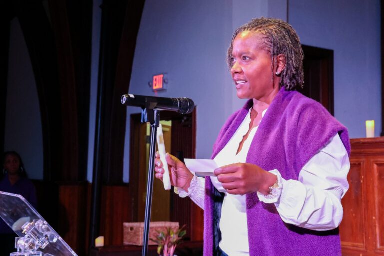 A speaker in purple reads from a card at the microphone