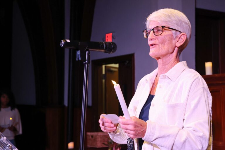 A speaker holds a candle while sharing remarks