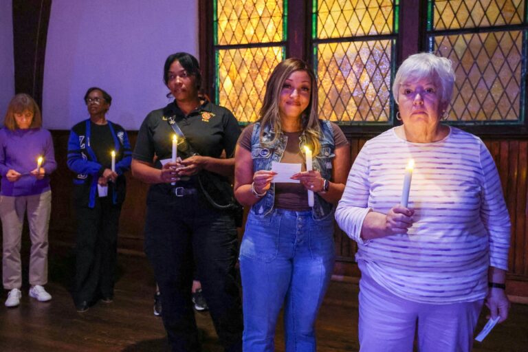 Candle bearers stand in line by the stained glass windows