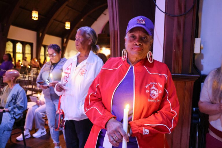 A candle bearer holds a lit candle in the aisle