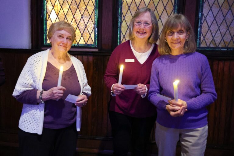 Three women hold candles and memorial cards
