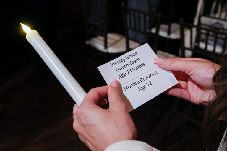 Hands hold a candle and a memorial card bearing the names of those lost