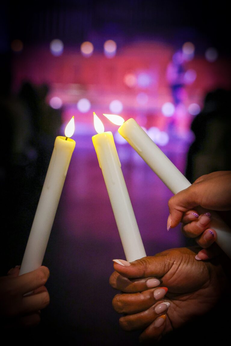 Attendees touch their candles together under soft purple light