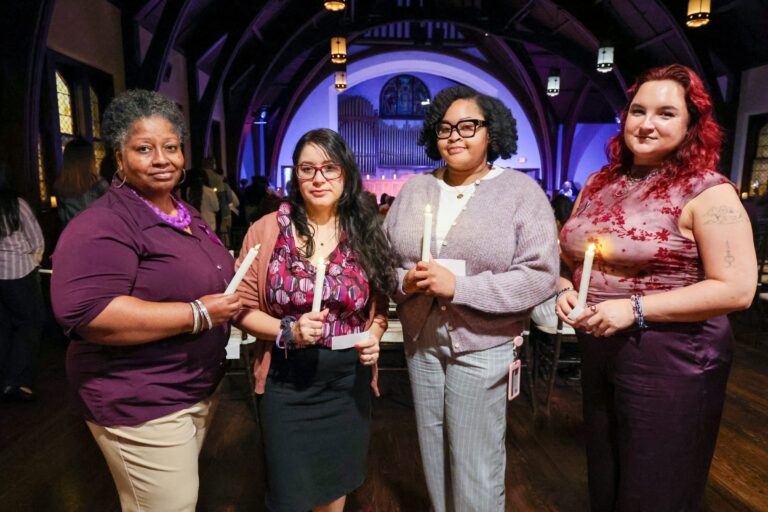 Four women stand together holding candles