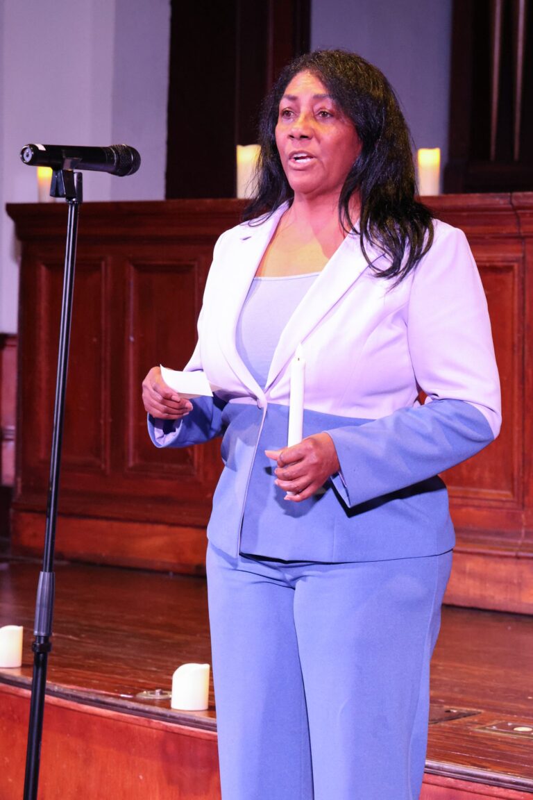 A speaker in a lavender suit addresses the gathering
