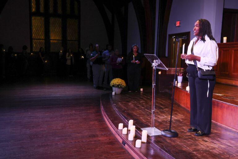 A speaker stands at the podium beside rows of candles
