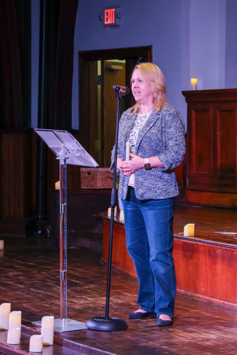 A speaker stands at a music stand to share remarks