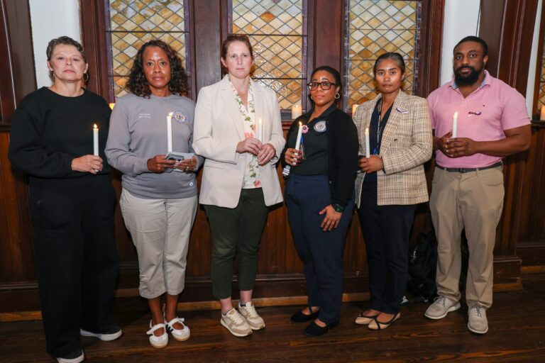 Six attendees stand together holding candles