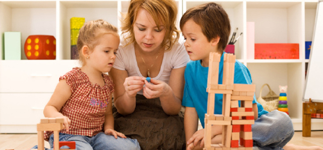 A mother building with wooden blocks alongside her two young children