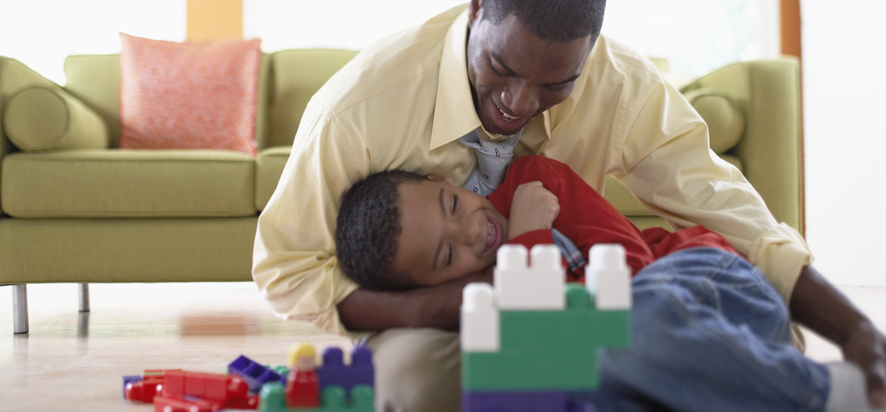 A father and his young son laughing together on the floor during a visit